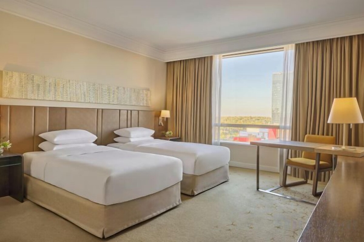 A hotel room with two beds, a desk, and a view of the city.