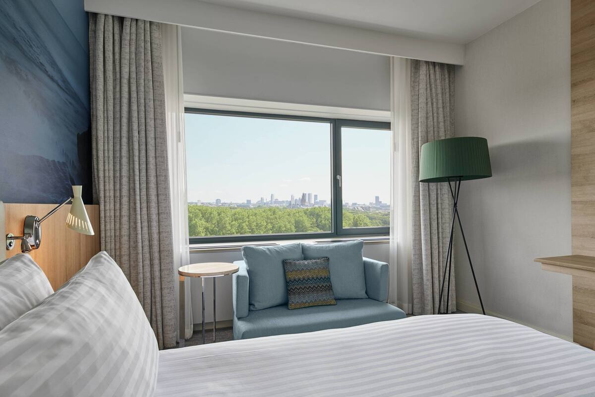 A hotel room with a bed, a small sofa with a view, a lamp, and a window with curtains.