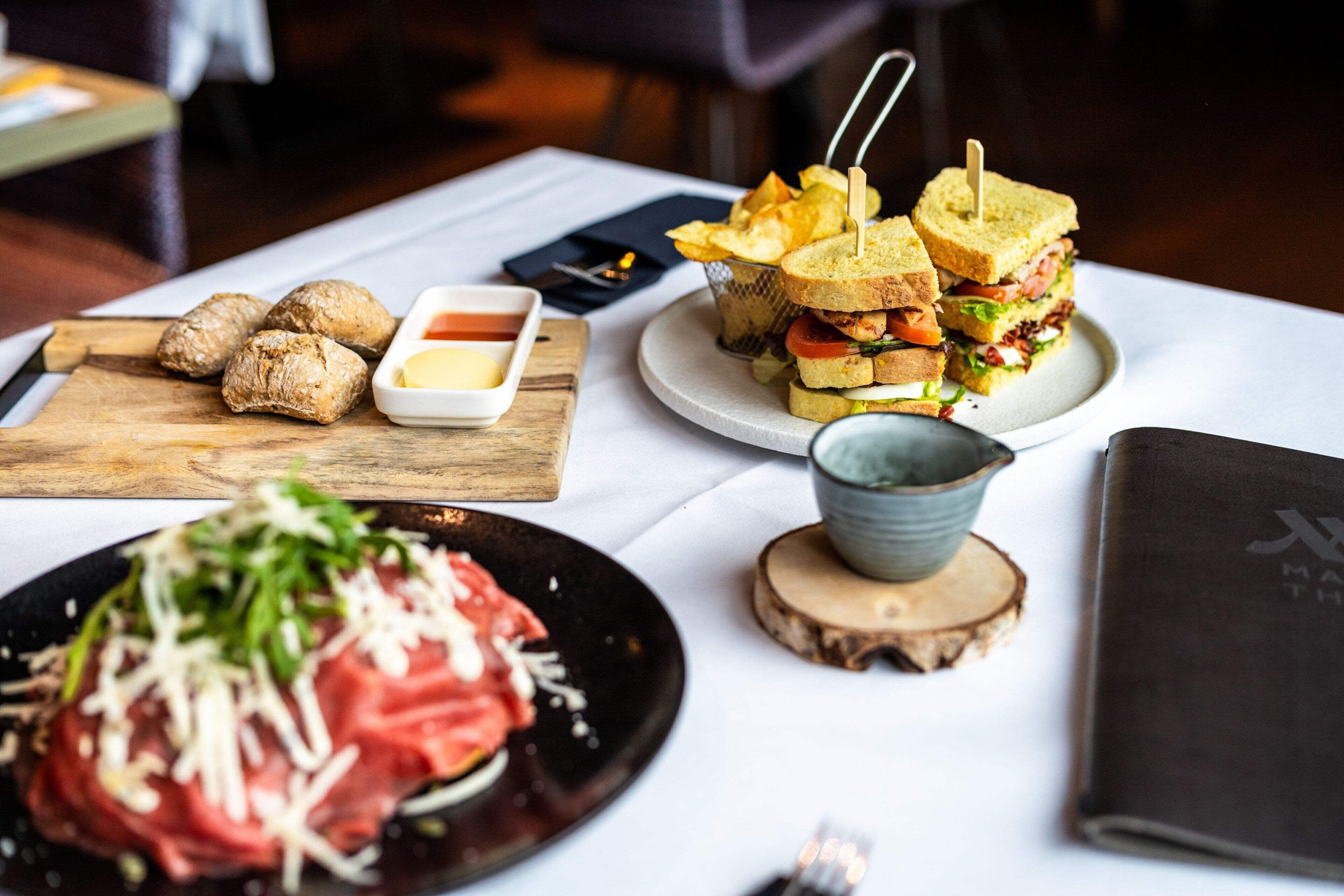 Een tafel met diverse etenswaren, waaronder sandwiches, een bord met rauw vlees en een klein schaaltje saus.