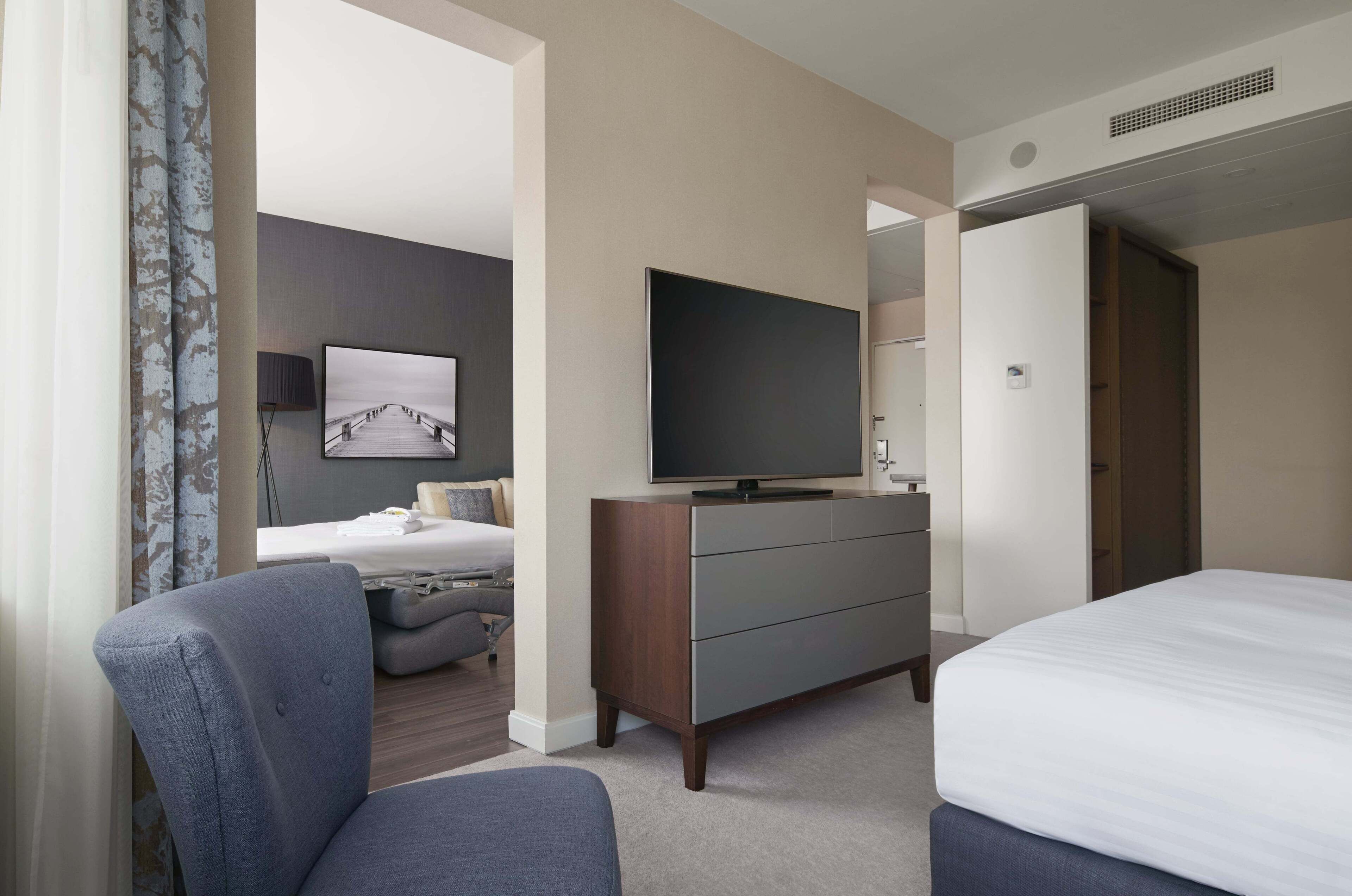 Hotellihuone, jossa on sänky, televisio, lipasto ja tuoli.