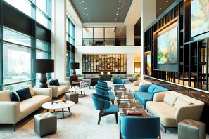 A spacious lobby with multiple seating areas, including sofas and armchairs, arranged around a central coffee table. - The Hague Marriott Hotel (The Hague)