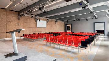 A conference room with rows of red chairs, a podium, and a projector screen.