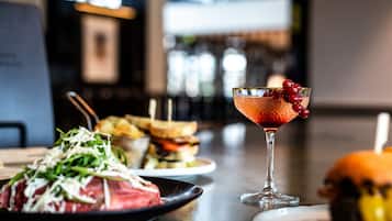Ein Esstisch mit einem Steakteller, einem Cocktailglas mit Beeren und Sandwiches im Hintergrund.