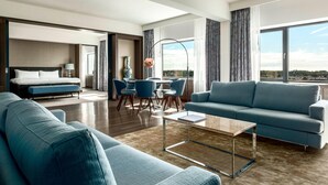 A modern hotel room with a large bed, a blue sofa, a dining area, and a view of the city. - The Hague Marriott Hotel (The Hague)