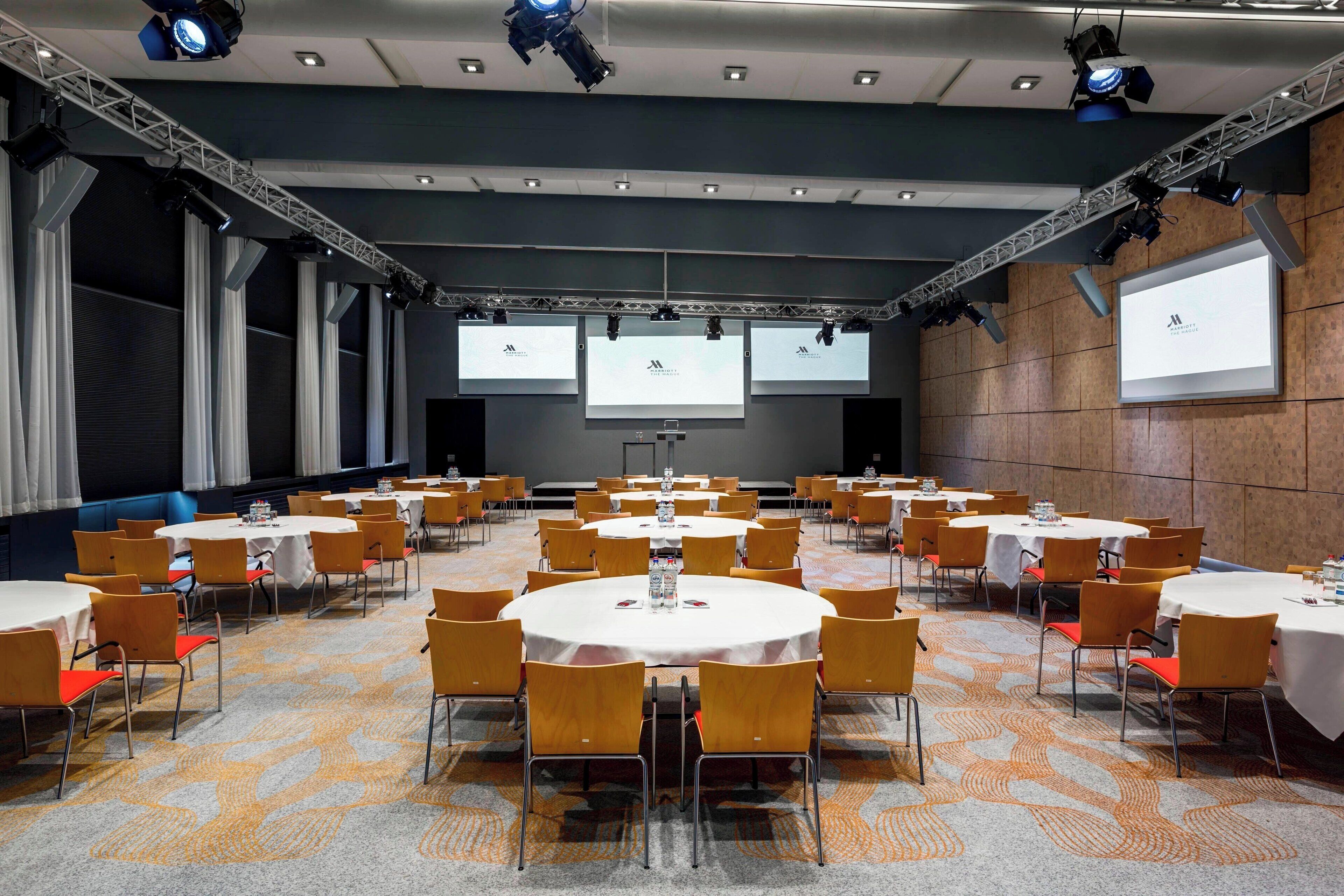 Una sala de conferències amb diverses taules rodones i cadires, equipada amb projectors i il·luminació.
