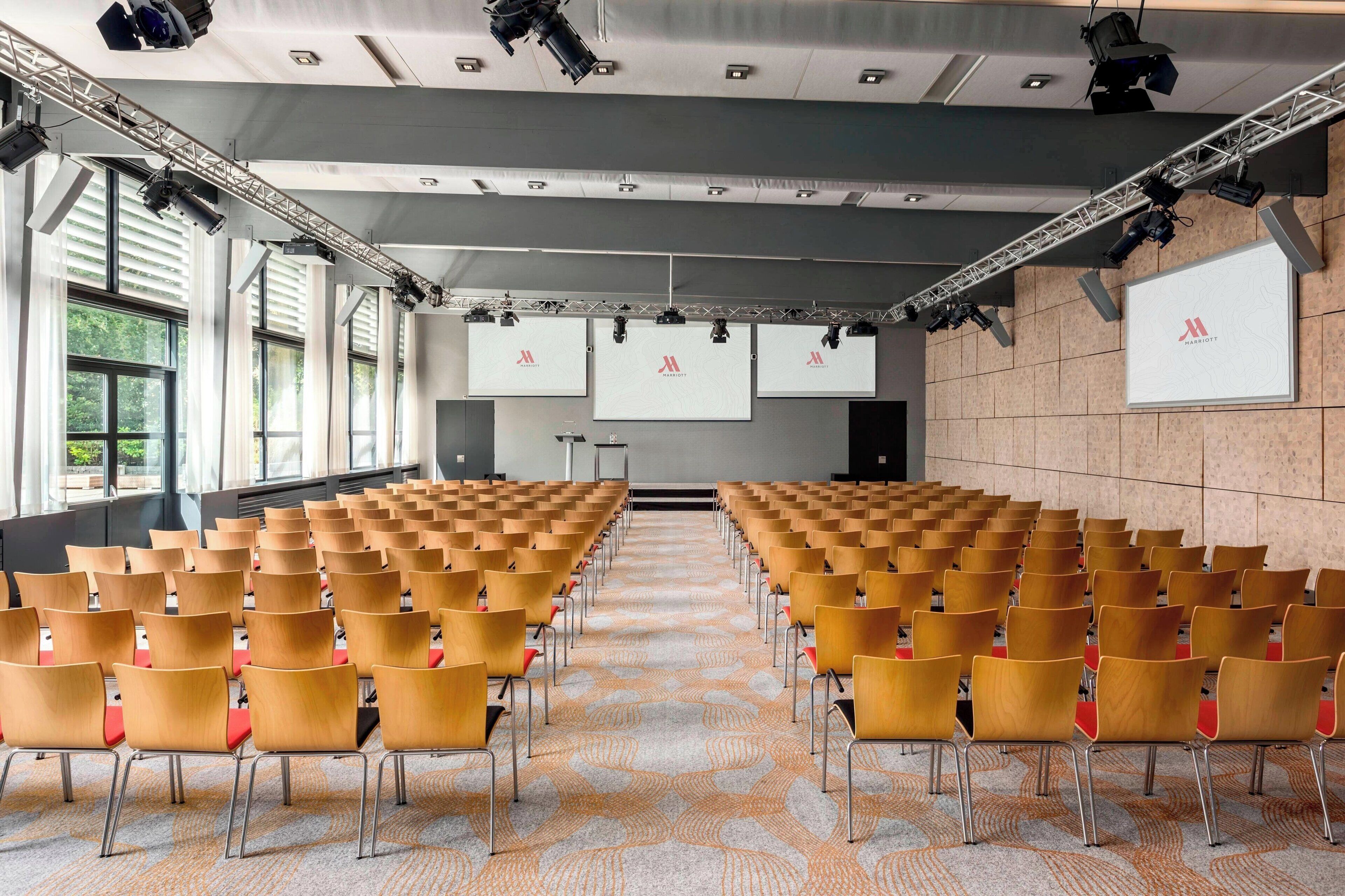 A conference room with rows of chairs, a stage with a screen, and large windows.