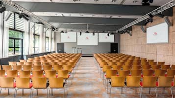 A conference room with rows of chairs, a stage with a screen, and large windows.