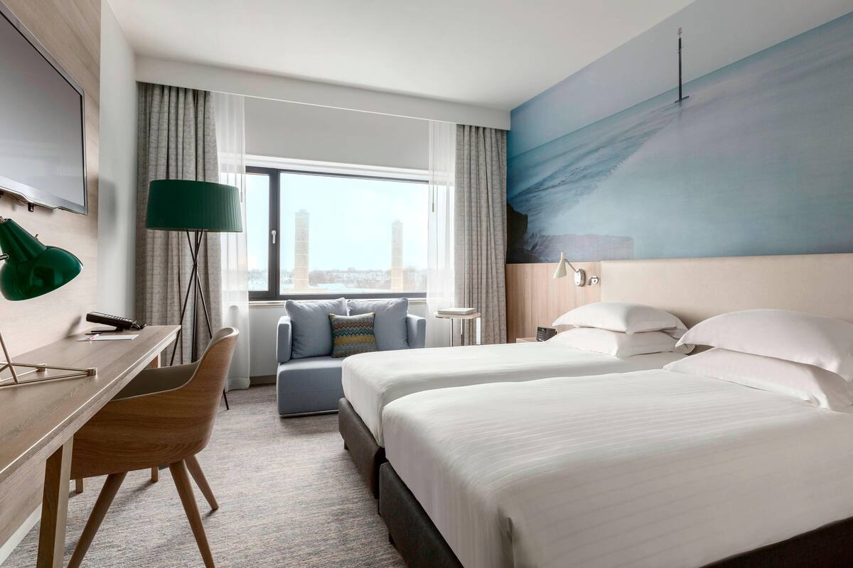 A hotel room with a large bed, a desk, a chair, and a view of the city.