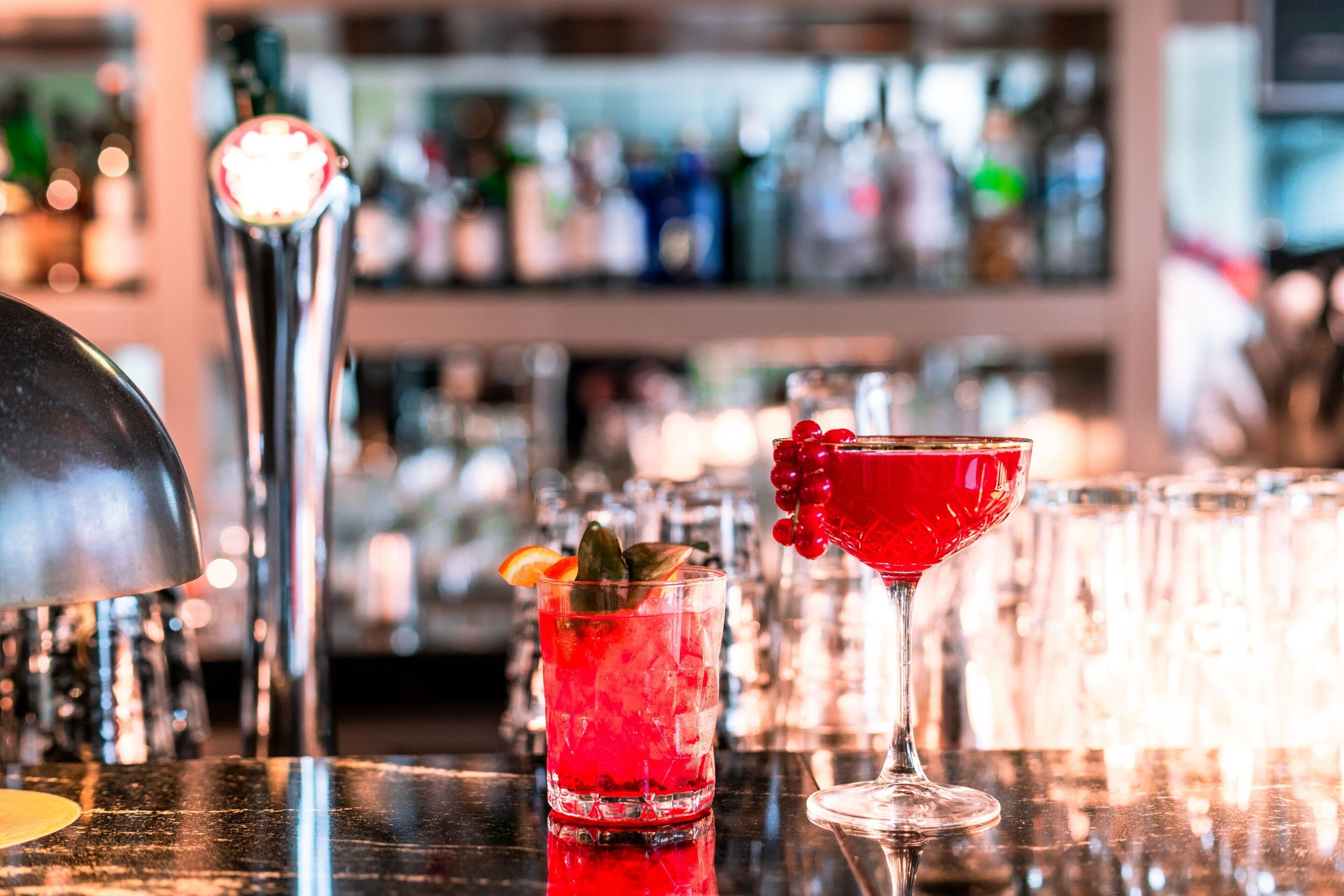 A bar setting with a variety of bottles and glasses, including a red cocktail and a martini glass.