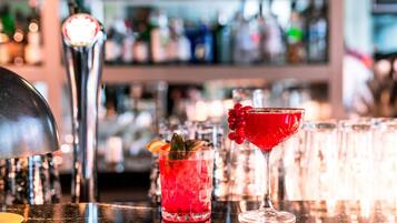 Un bar con una variedad de botellas y vasos, incluyendo un cóctel rojo y una copa de martini.