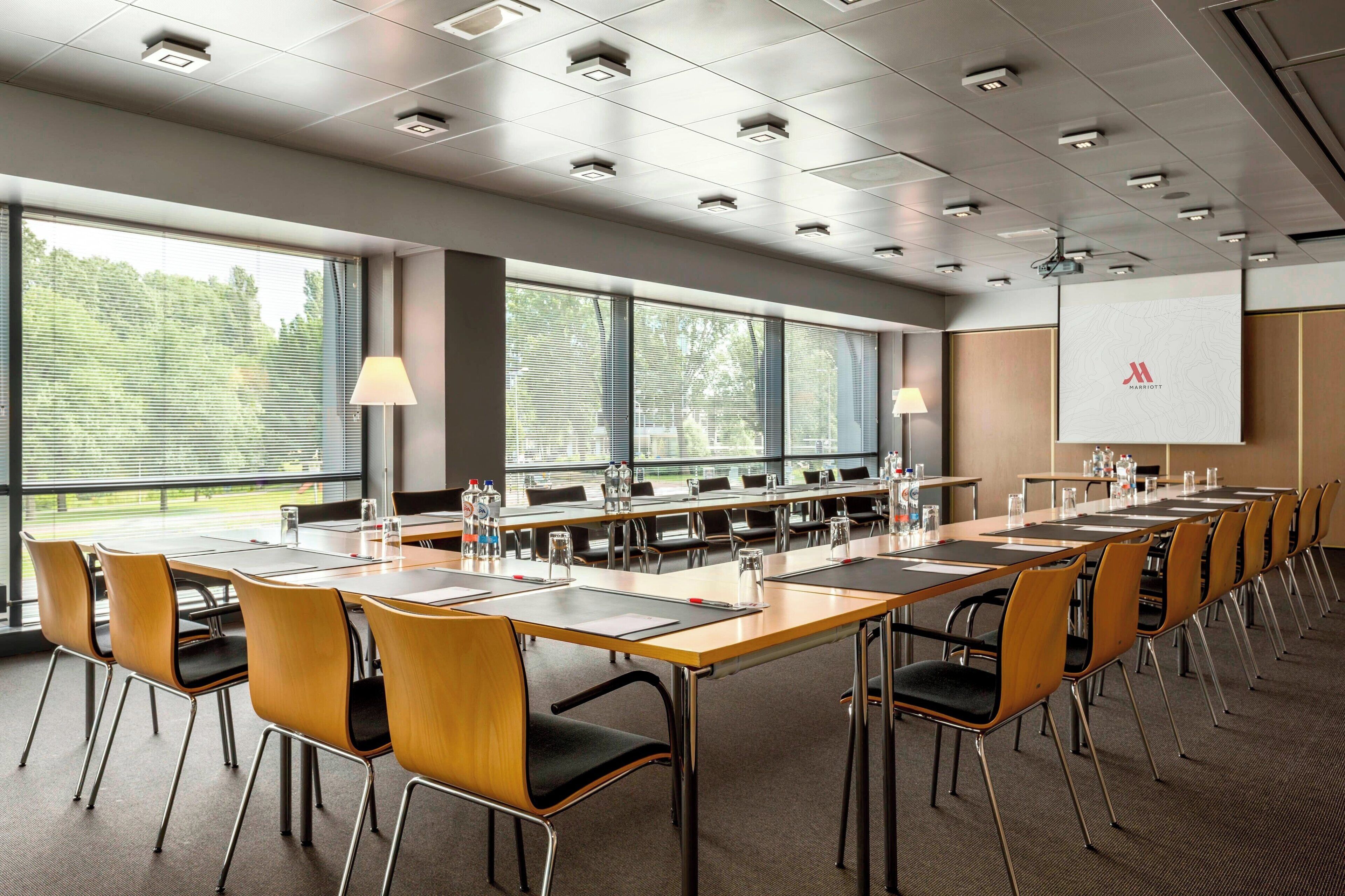 A conference room with a long table, chairs, and a projector screen.