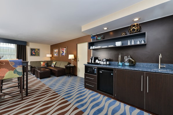 A hotel room with a kitchenette, a sofa, a dining table, and a patterned carpet.