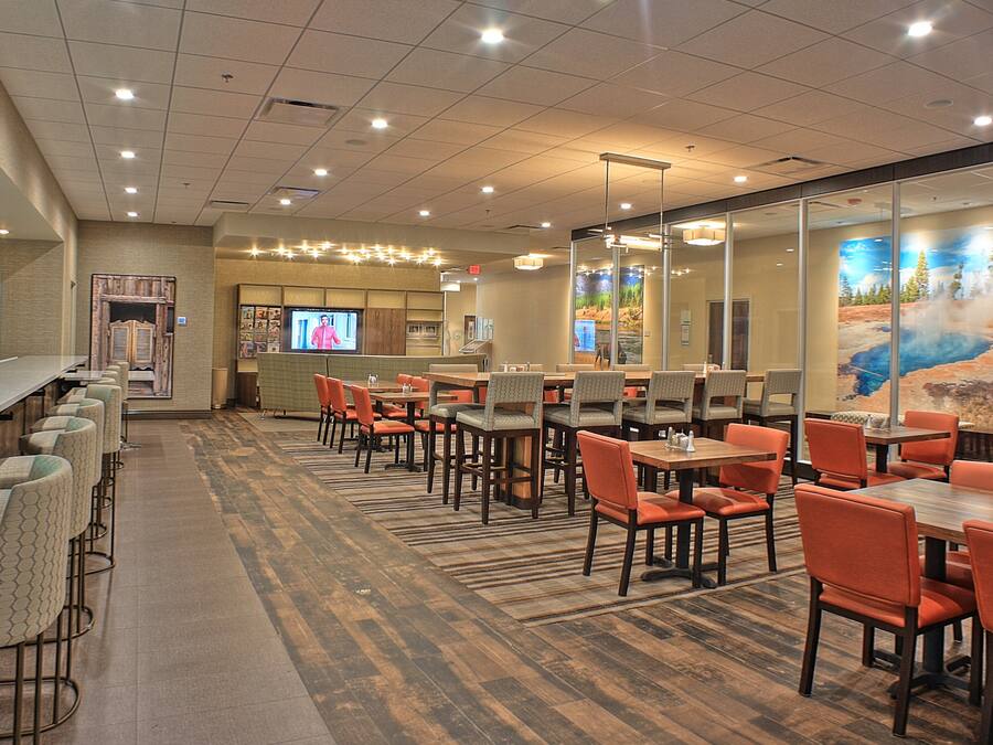 A restaurant with multiple tables and chairs, a bar area, and a television screen.