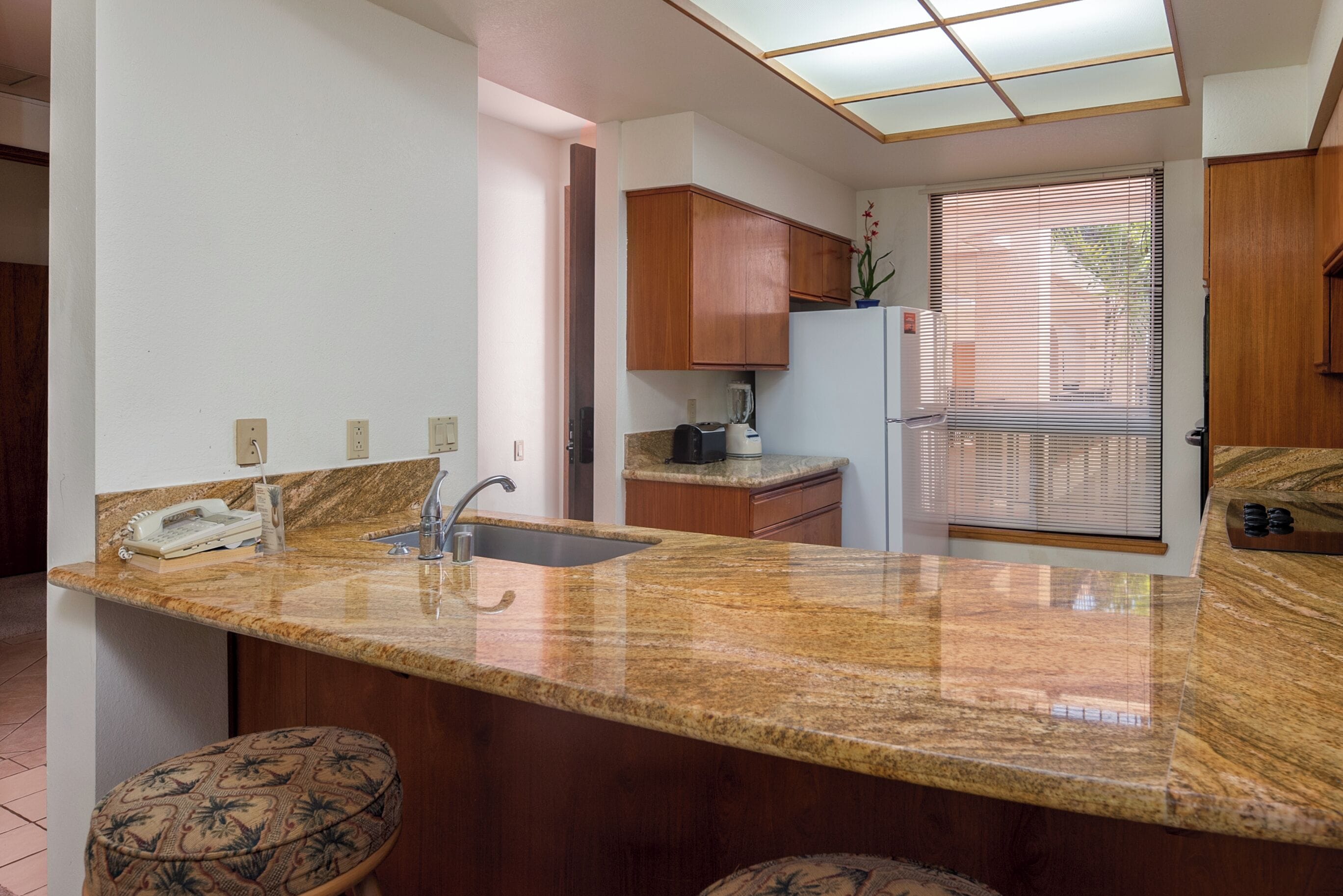 A kitchen with granite countertops, wooden cabinets, a built-in sink, and a window with blinds.