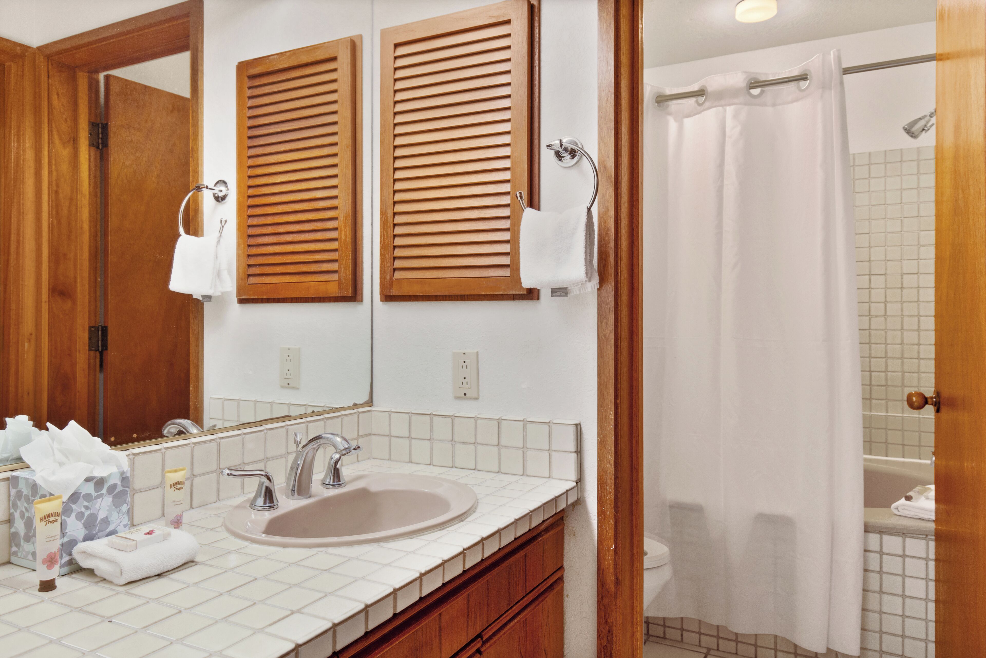 A bathroom with a sink, mirror, wooden shutters, and a shower curtain.