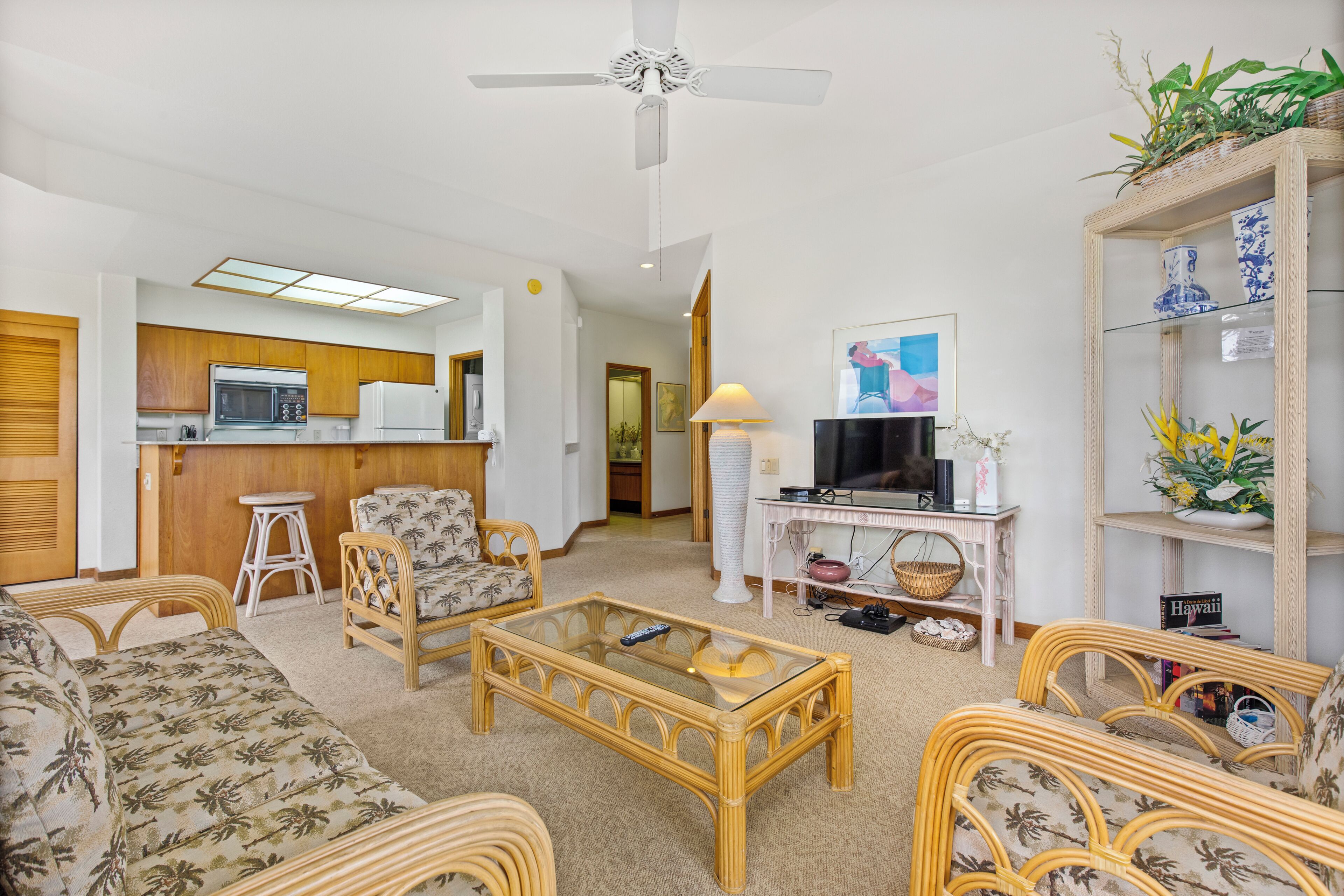 A living room with a sofa, two armchairs, a coffee table, a TV, a bookshelf, and a kitchen area with a microwave and refrigerator.