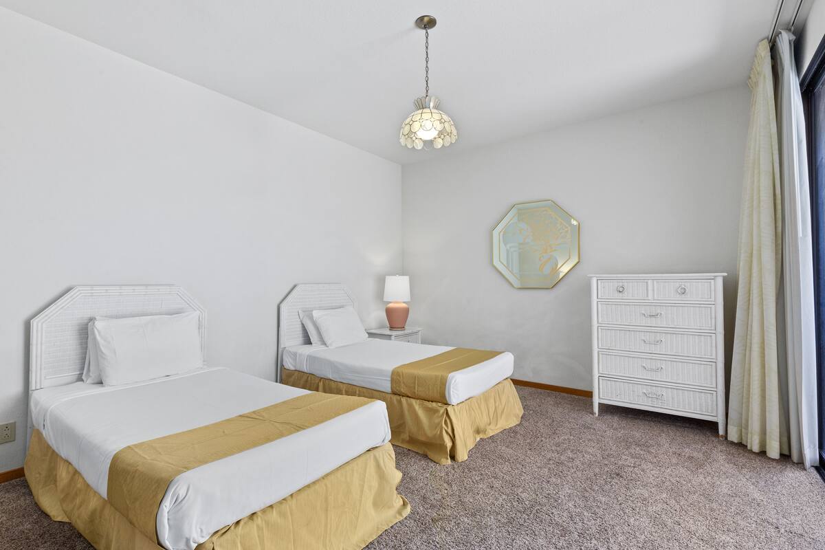 A hotel room with two beds, a dresser, a lamp, and a decorative mirror.