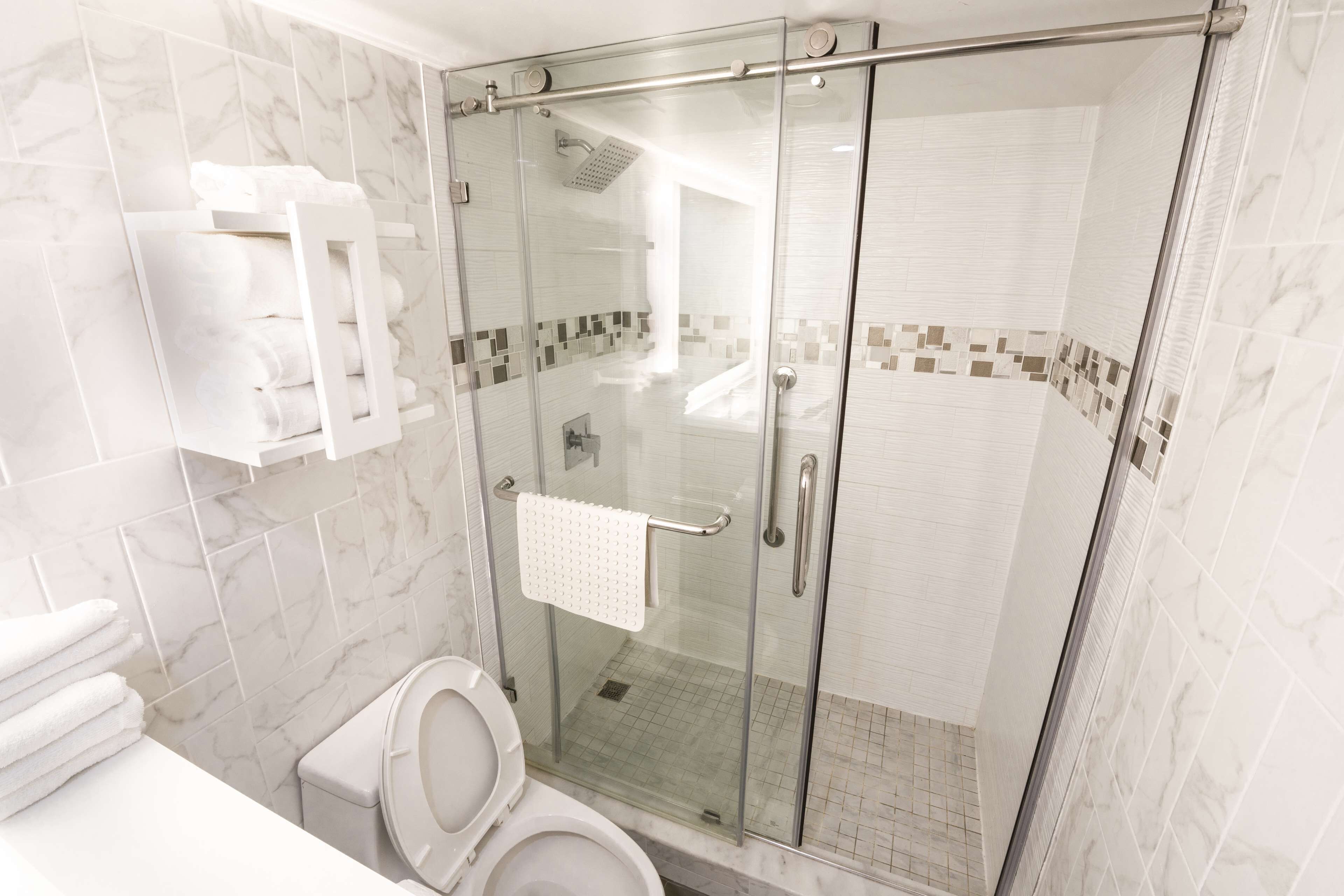 A modern bathroom with a glass-enclosed shower, a toilet, and a towel rack with folded towels.