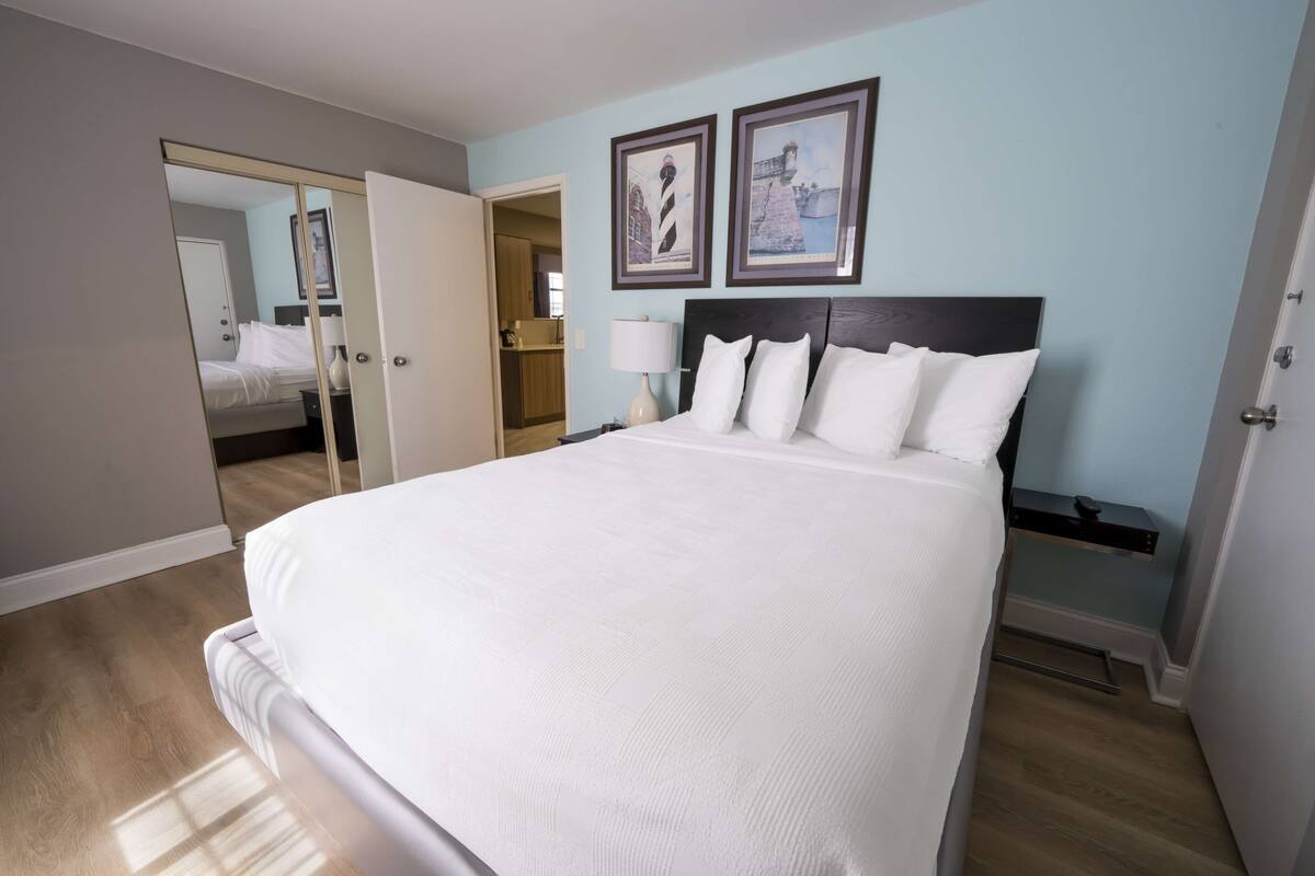 A hotel room with a large bed, a nightstand, a mirror, and two framed pictures on the wall.