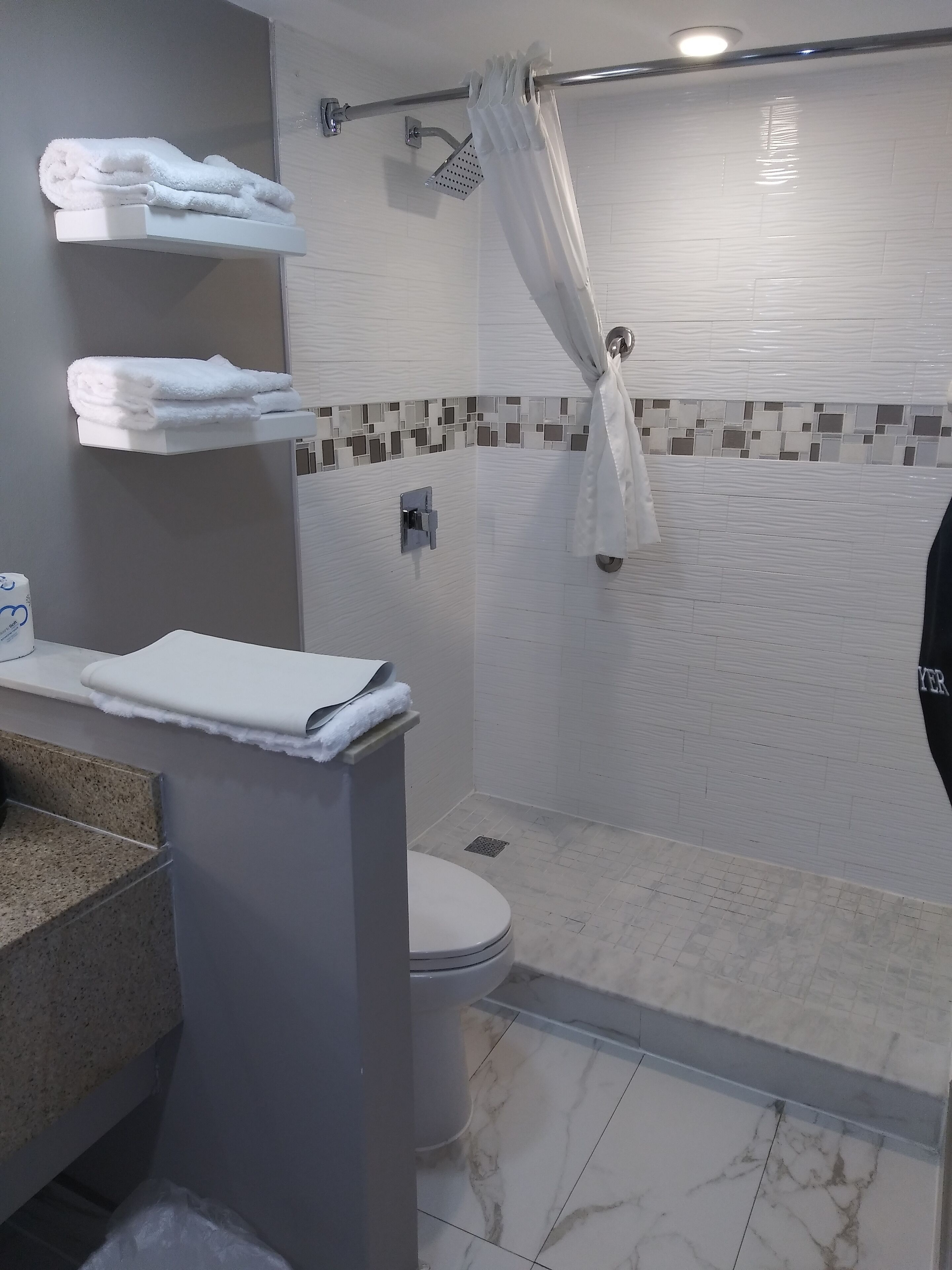 A modern bathroom with a shower, toilet, and a towel rack with folded towels.