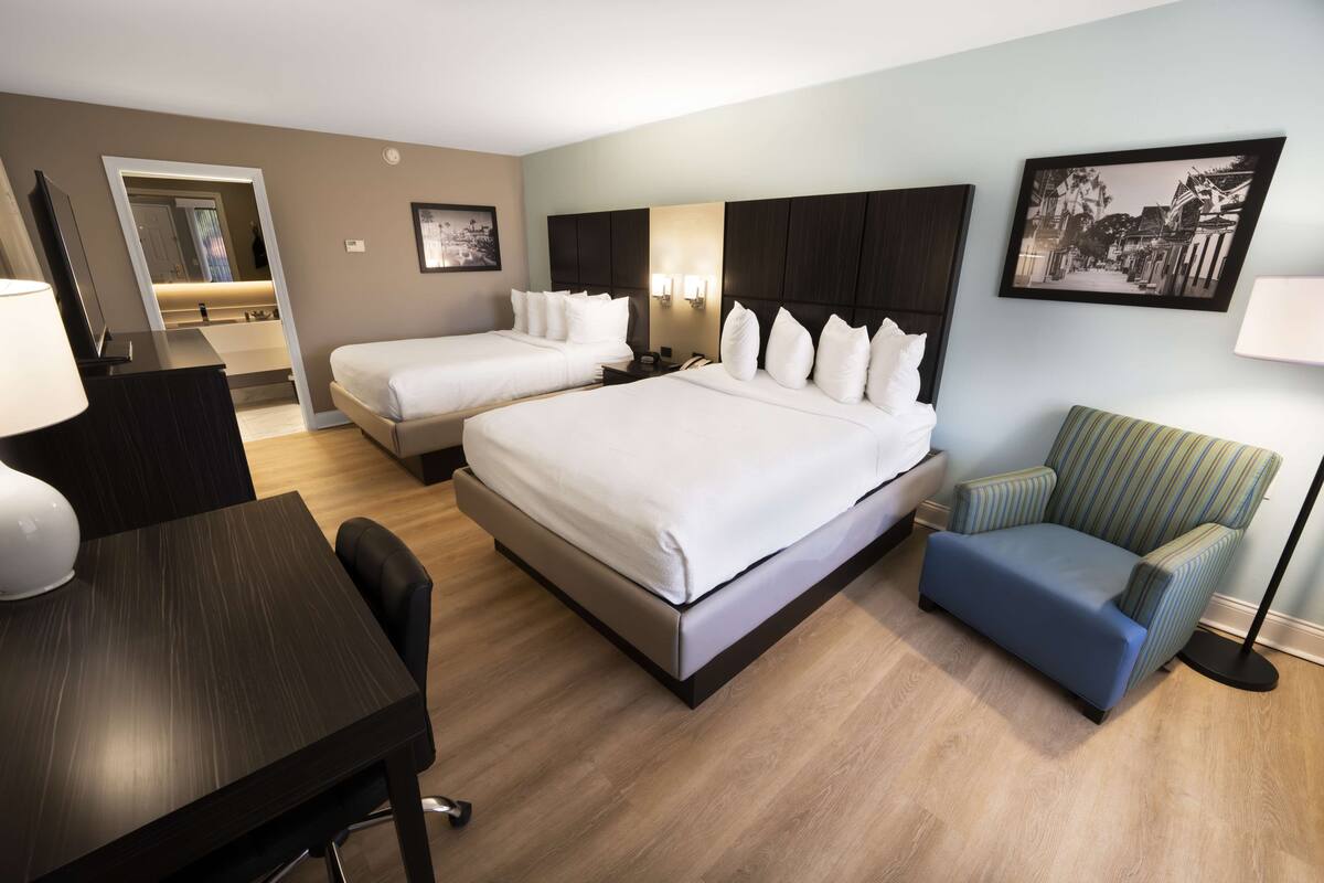 A hotel room with two beds, a desk, a chair, and a lamp.