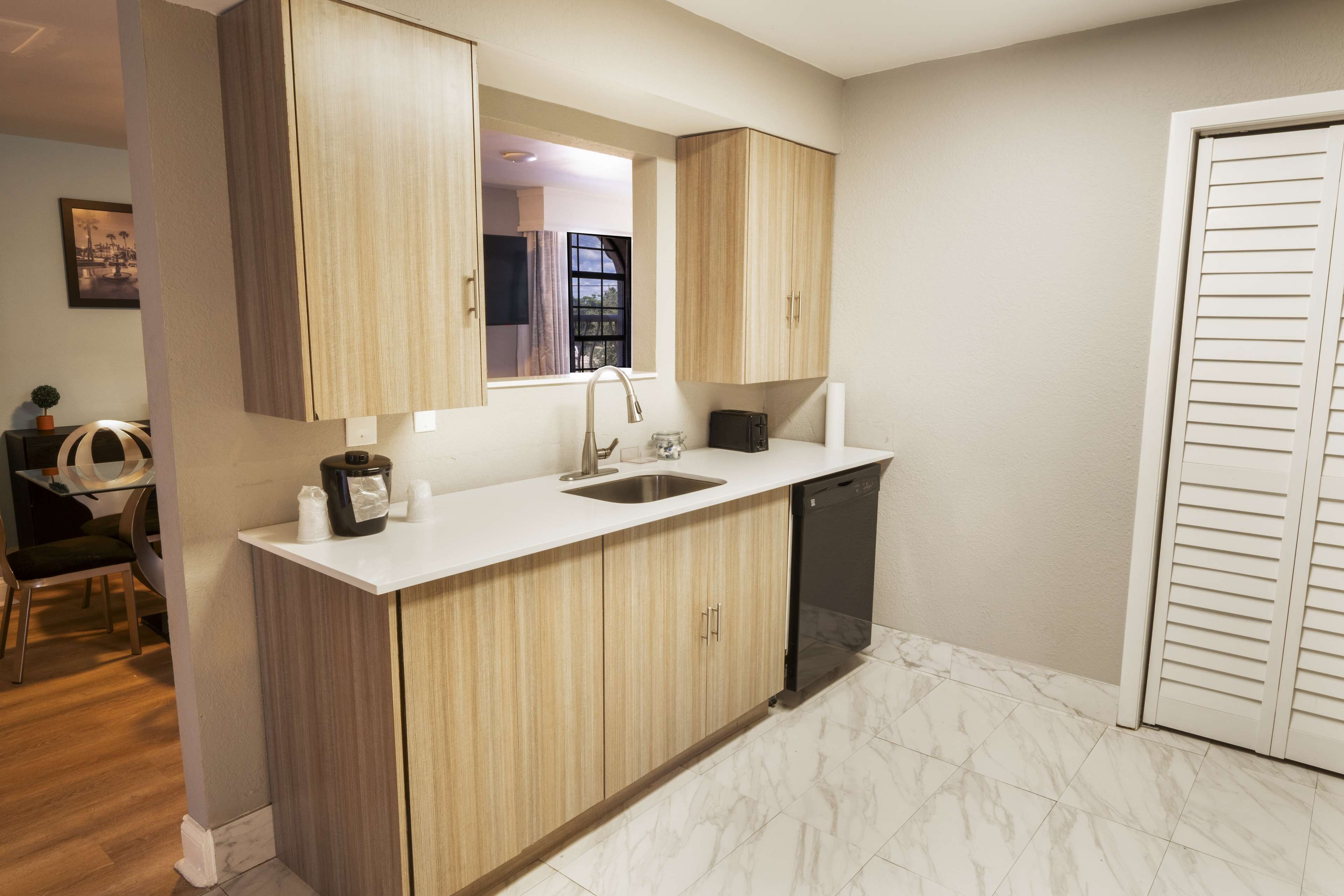 A modern kitchen with wooden cabinets, a white countertop, a dishwasher, and a window with a view of the outdoors.
