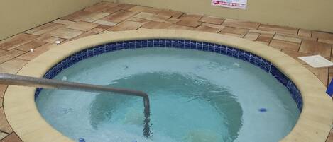 Un jacuzzi con borde de azulejos y un cartel con las normas del spa.
