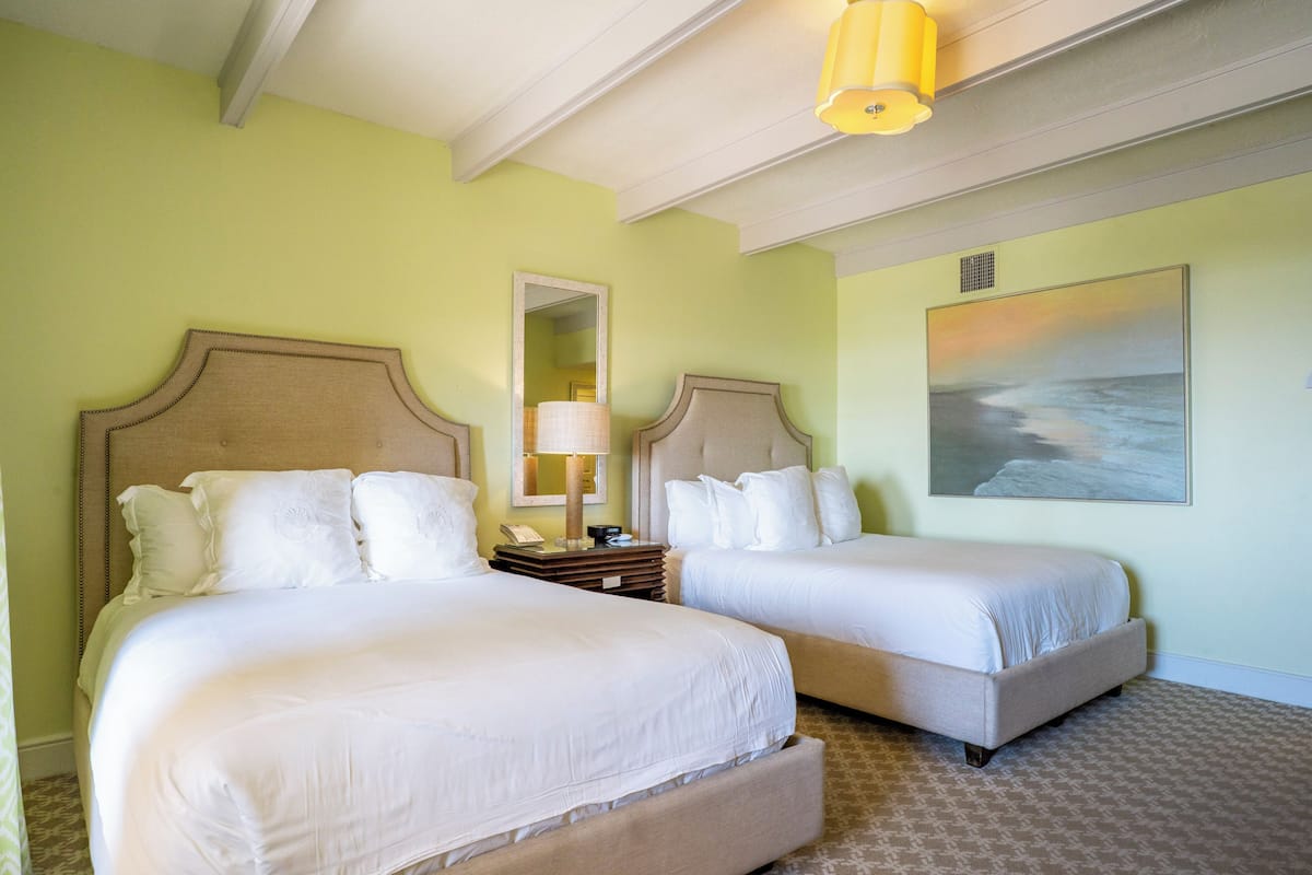 Une chambre d’hôtel avec deux lits, un miroir, une lampe et un tableau au mur.