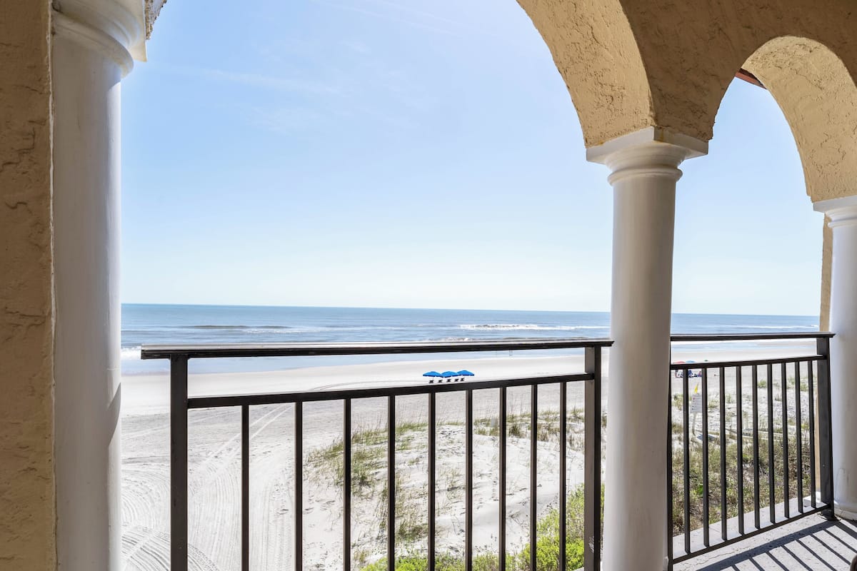 Un balcon donnant sur la plage, avec des colonnes blanches et une balustrade.