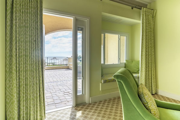 Una habitación con una silla verde, una ventana con vistas y una puerta que da a un área exterior.