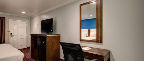 Habitación de hotel con cama, escritorio, silla, televisor y espejo.