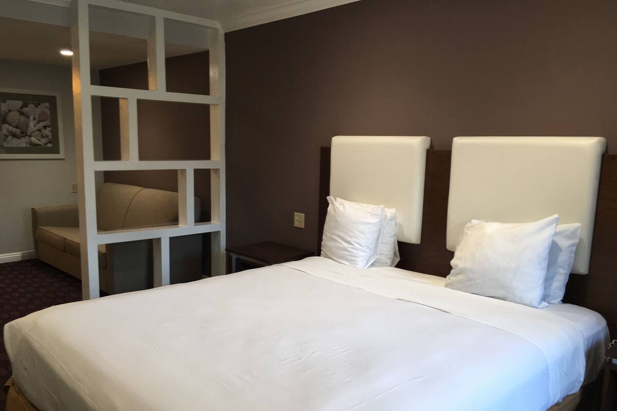 A hotel room with a large bed, white bedding, a small bedside table, and a wall-mounted light fixture.
