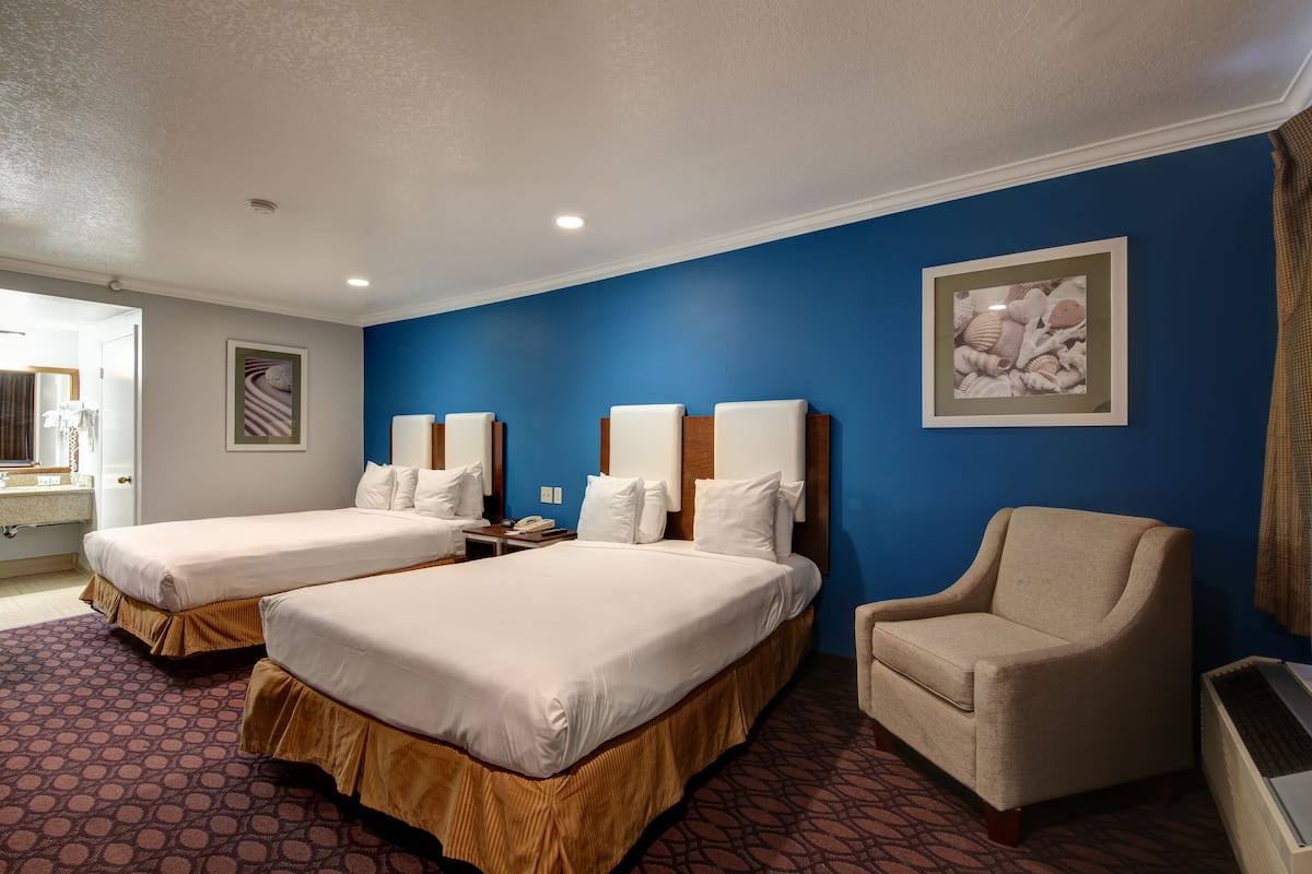 A hotel room with two beds, a chair, a desk, and a framed picture on the wall.