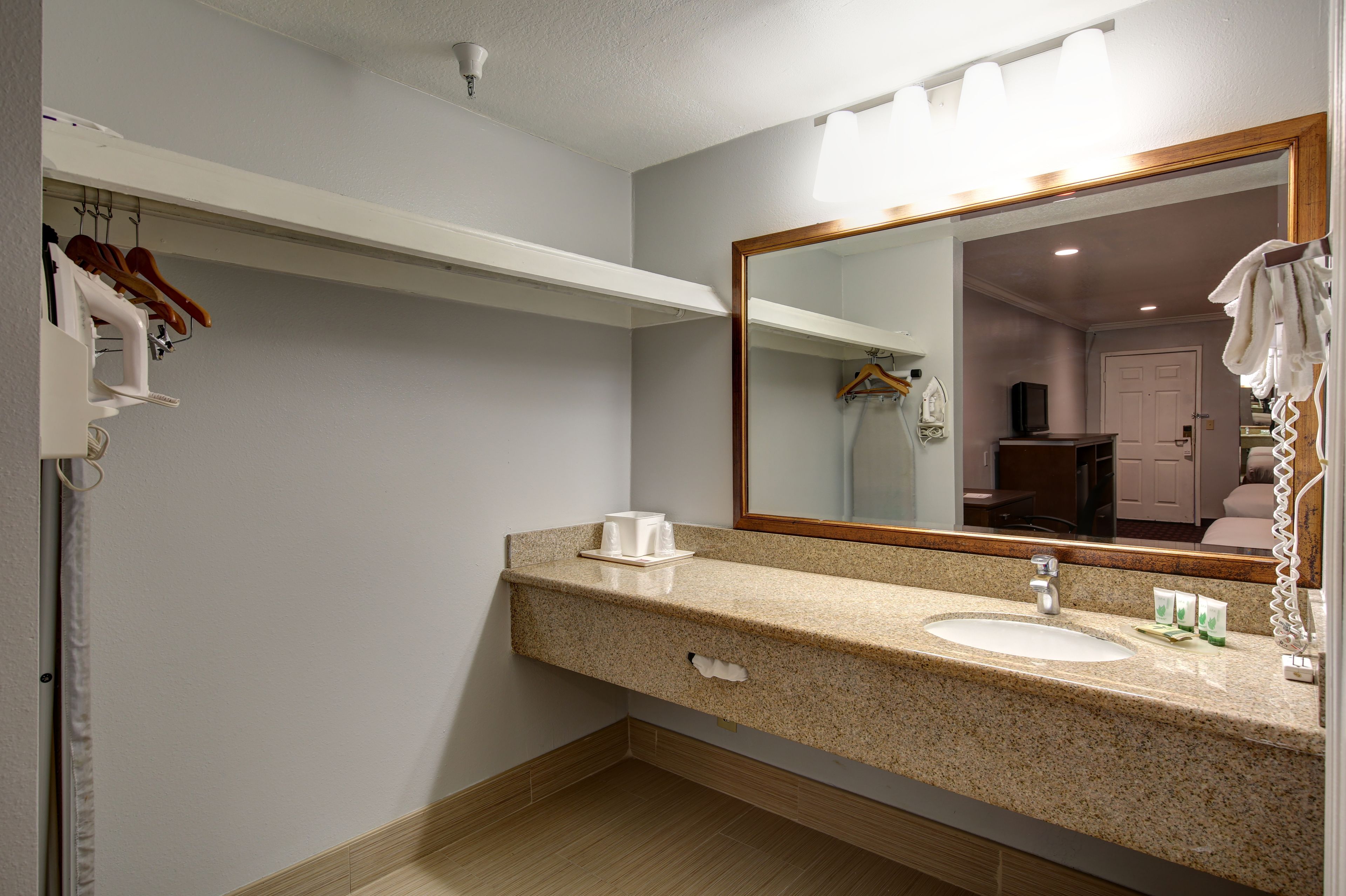 Baño con lavamanos de encimera de granito, un espejo con iluminación, un perchero y una zona de ducha visible en el reflejo.