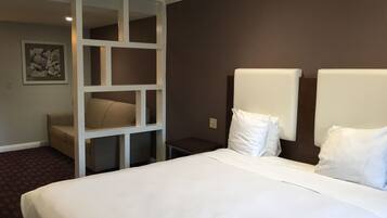 A hotel room with a large bed, a seating area with a sofa and a white partition, and a framed picture on the wall.