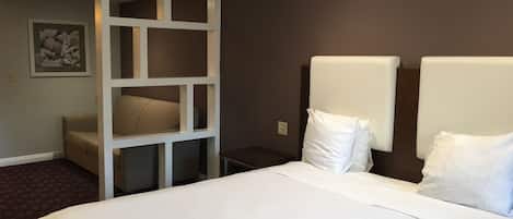 A hotel room with a large bed, a seating area with a sofa and a white partition, and a framed picture on the wall.