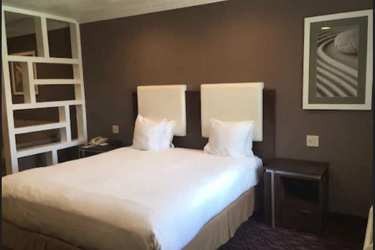 A hotel room with a large bed, two bedside tables, a nightstand, and a built-in shelving unit.