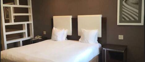 A hotel room with a large bed, two bedside tables, a nightstand, and a built-in shelving unit.