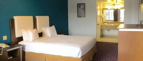 Una habitación de hotel con cama, mesitas de noche, escritorio, espejo y baño con lavamanos y espejo.