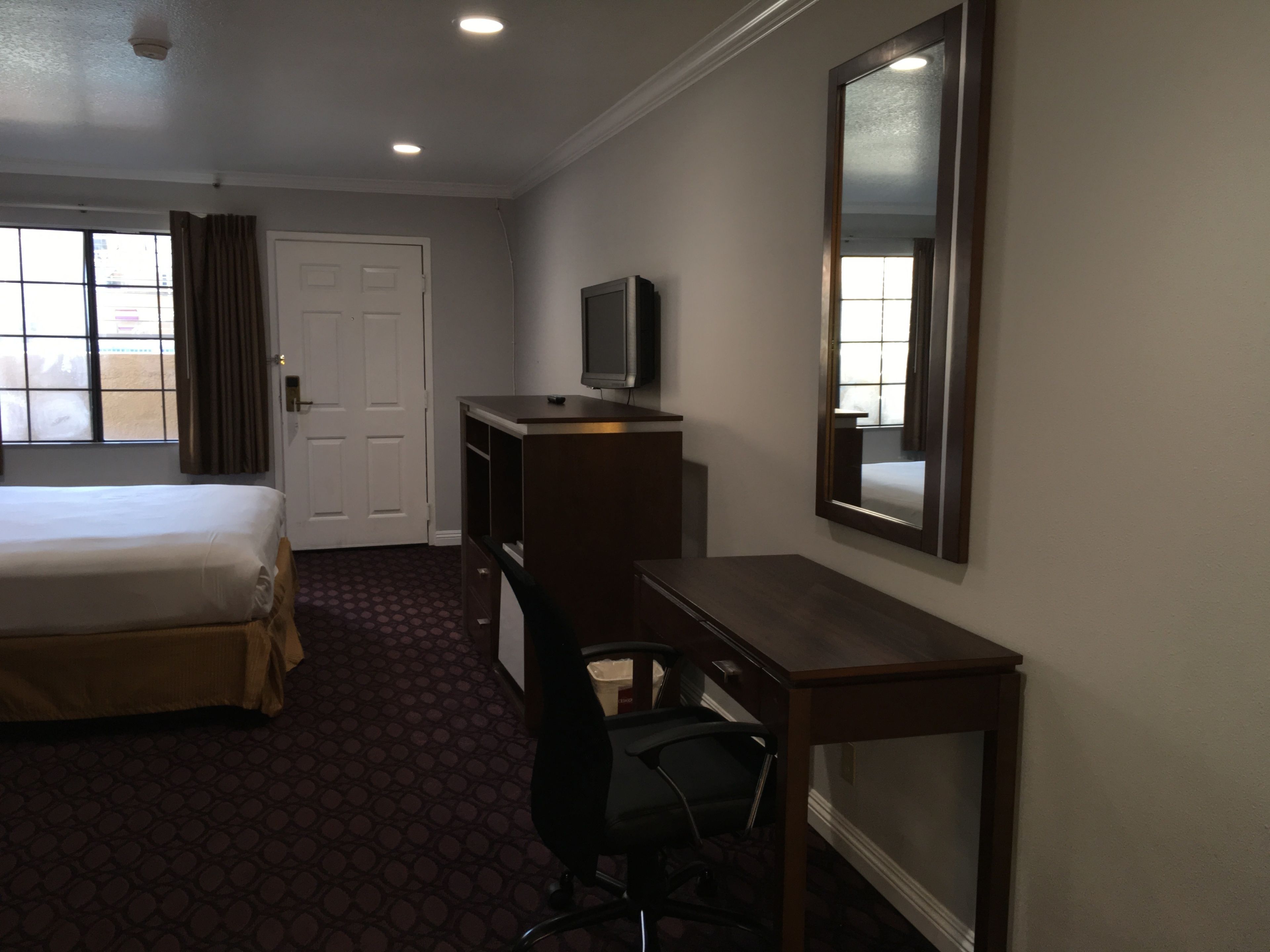 Una camera d'albergo con un letto, una scrivania, una sedia, un televisore e uno specchio grande.