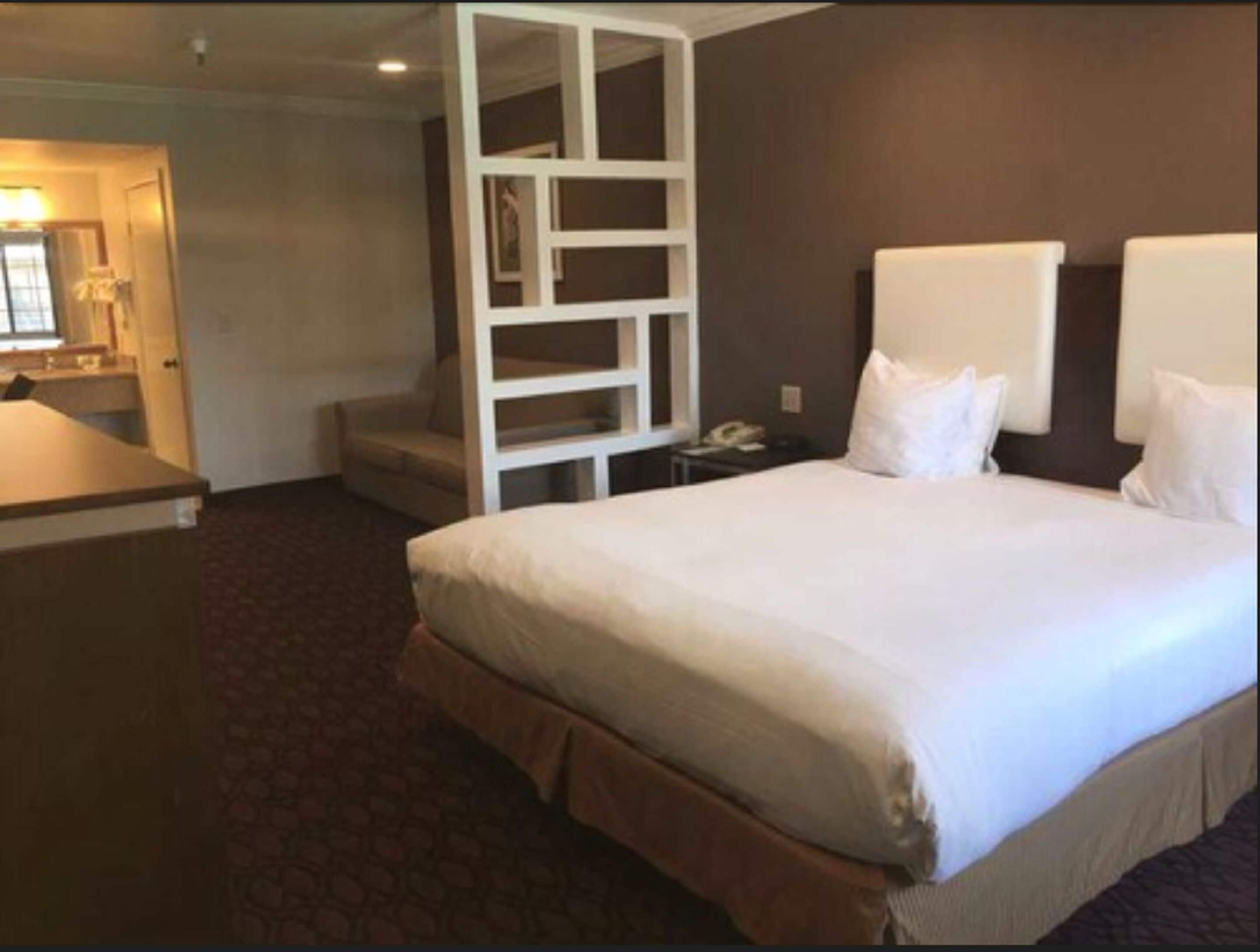 A hotel room with a large bed, a desk, and a built-in shelving unit.