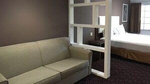 Une chambre d’hôtel avec un canapé beige, un lit recouvert d’une couette blanche et une fenêtre avec des rideaux.