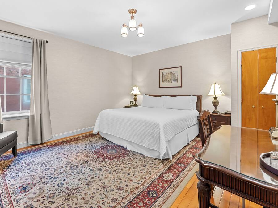 Habitación de hotel con una cama grande, dos lámparas de noche, piso de madera, alfombra estampada, ventana con cortinas y puerta con espejo.