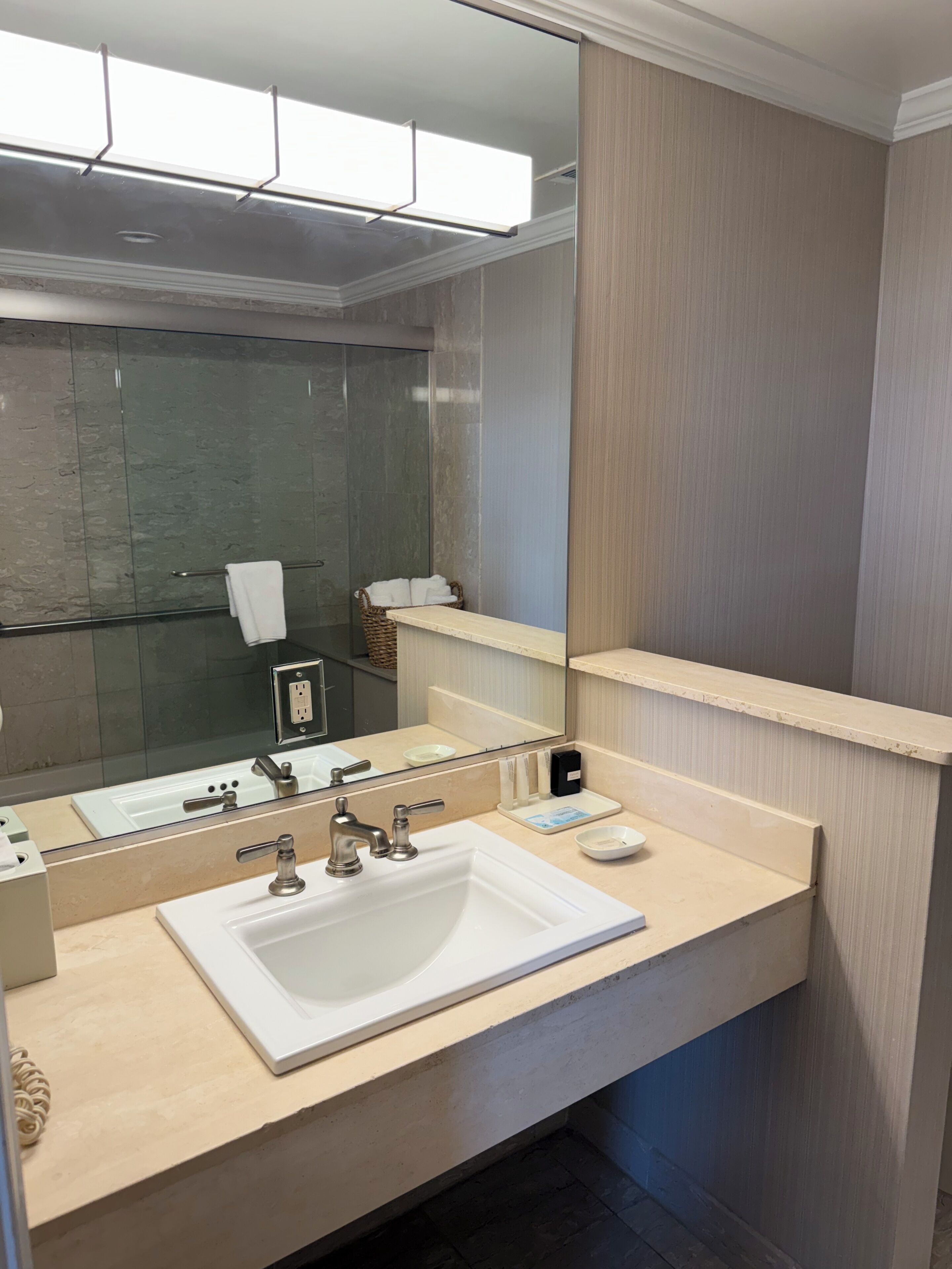 Une salle de bain moderne avec un grand miroir, un lavabo blanc, un porte-serviettes et un espace douche.
