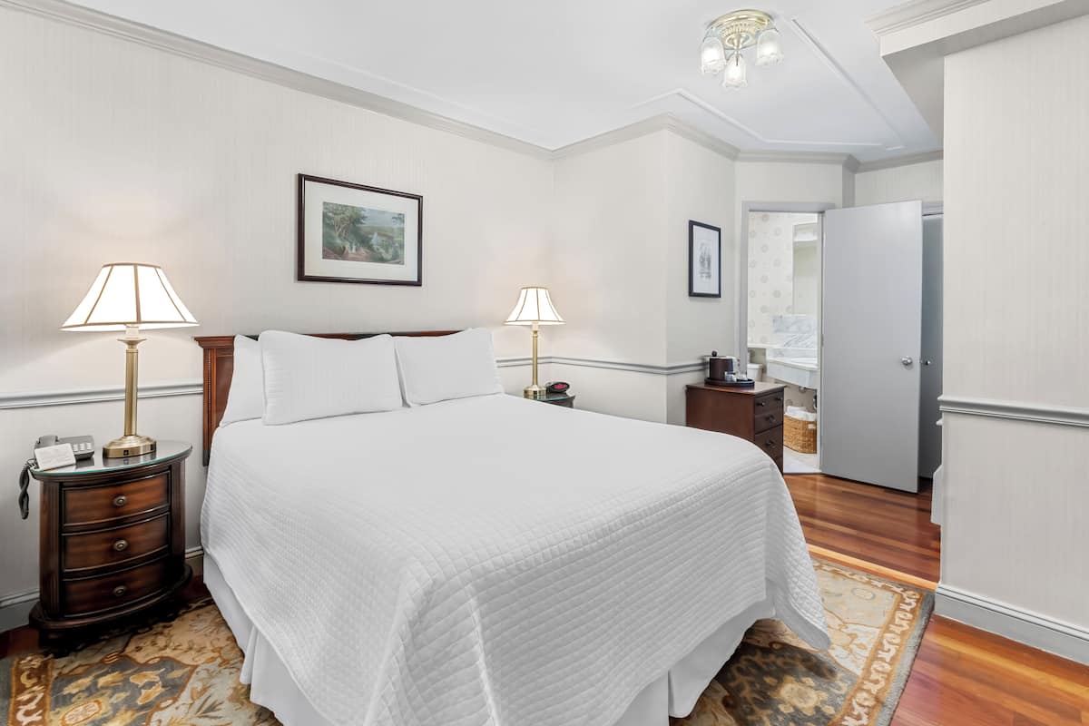 A hotel room with a large bed, two bedside tables with lamps, a framed picture on the wall, and a wardrobe.