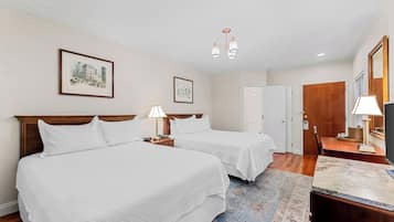 Habitación de hotel con dos camas, un escritorio, una silla, una lámpara, un espejo y dos cuadros colgados en la pared.