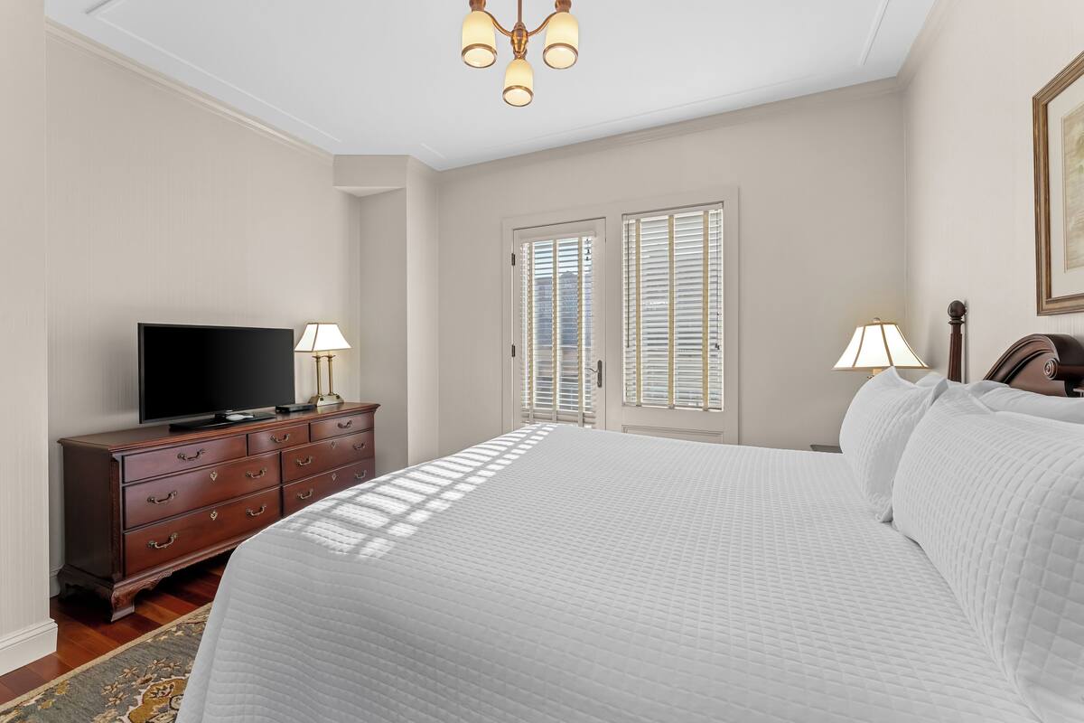 A bedroom with a large bed, a dresser, a television, and two lamps.