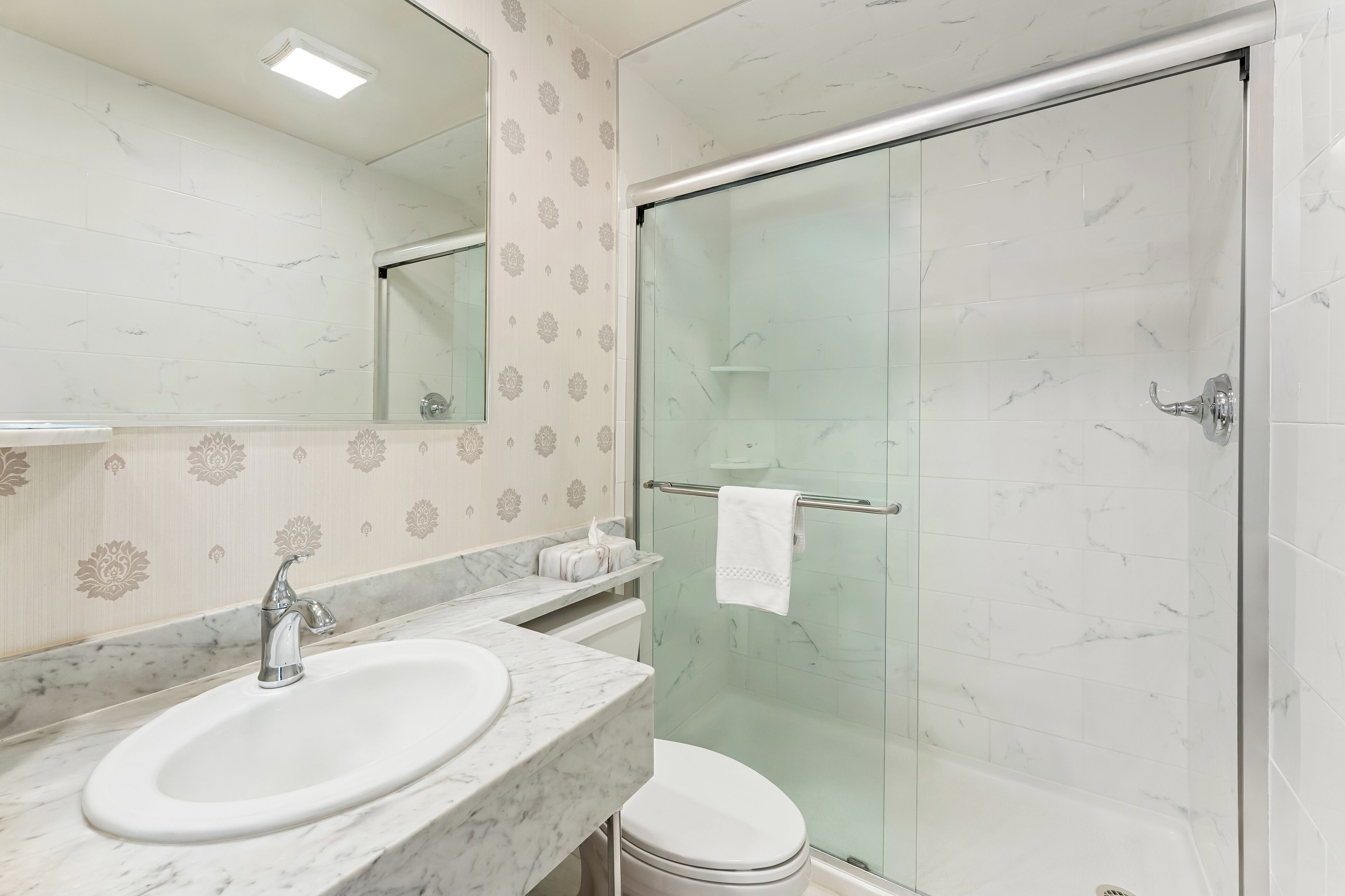 Un baño con lavamanos de mármol, cabina de ducha con vidrio y retrete.