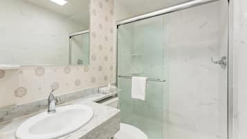 Un baño con lavamanos de mármol, cabina de ducha con vidrio y retrete.