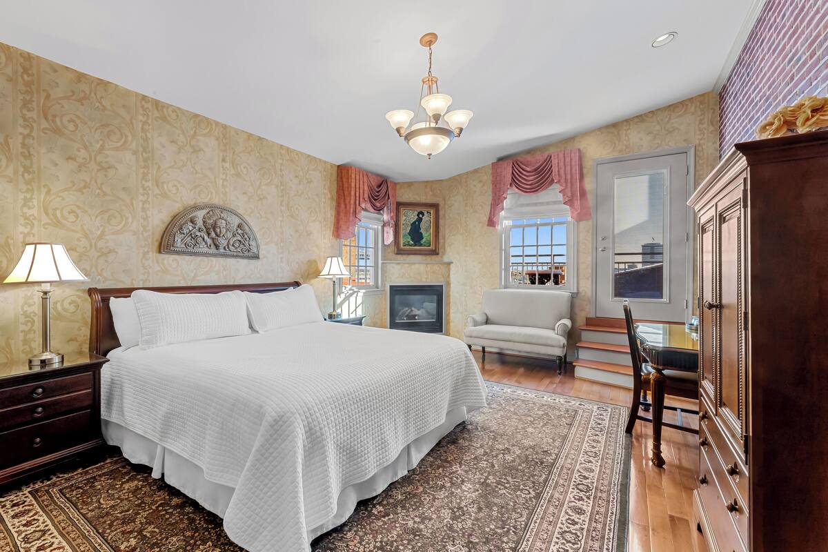 A bedroom with a large bed, a dresser, a chair, a fireplace, and a chandelier.